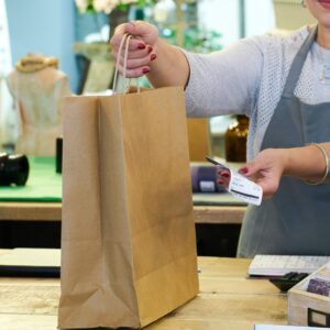 Cropped shot of sales assistant handing shopping bag and receipt at gift shop checkout