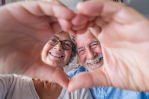 Close up portrait happy sincere middle aged elderly retired family couple making heart gesture